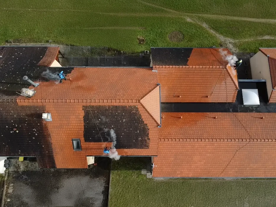 Vue aérienne de toiture résidentielle en tuiles terre cuite avec ouvriers effectuant travaux de rénovation