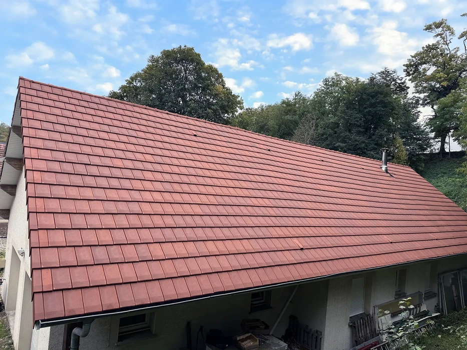 Toiture résidentielle en tuiles de terre cuite rouge récemment rénovée sous ciel bleu avec végétation environnante