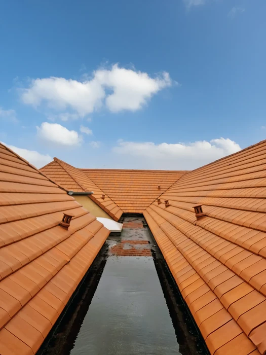 Vue extérieure d'une toiture en tuiles terre cuite orangées avec système de gouttière centrale