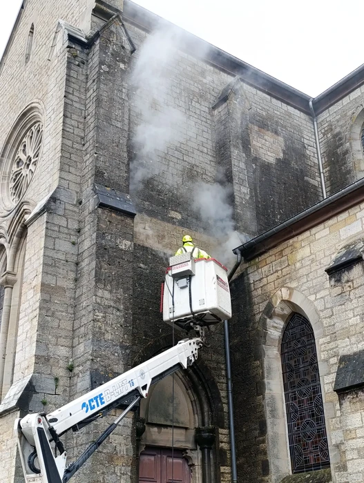 Intervention de nettoyage sur façade d'église historique en pierre calcaire avec nacelle élévatrice hydraulique