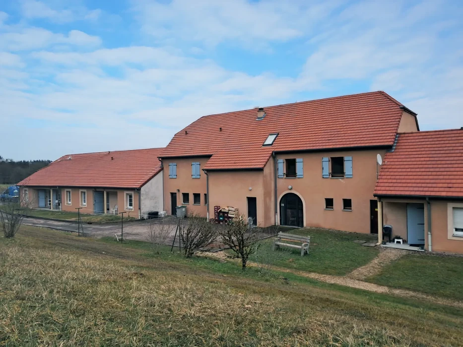 Extérieur d'une maison individuelle avec façade en bardage bois peint gris-bleu, toiture en tuiles terre cuite et fenêtres blanches à double vitrage