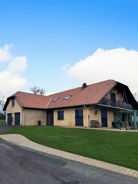 Maison en bois massif de style chalet avec bardage horizontal brun foncé, équipée de volets battants orange, fenêtres à double vitrage PVC blanc et terrasse couverte