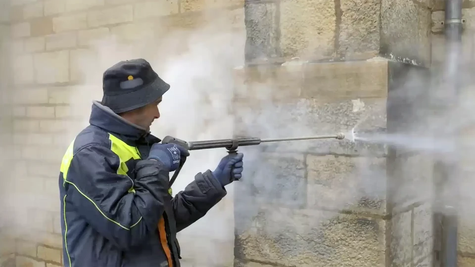 Façade extérieure en pierre naturelle grise avec joints blancs, fenêtre protégée par grille de sécurité en fer forgé noir à barreaux verticaux et motifs décoratifs courbes